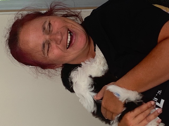 A smiling woman cuddling a small black-and-white dog